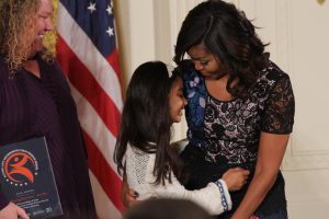 Sarah Hussein, 11, hugs the First Lady during the award ceremony. Hussein is part of 'The Reading Road Show - Gus Bus' a program that brings children's literature to children in low-income neighborhoods (Kelly Norris/MNS).