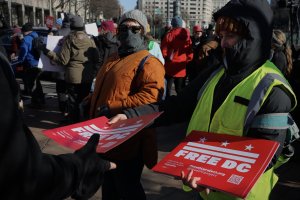 A participant hands out “Free DC” signs to demonstrators as crowds continue to grow during the rally. (André Hiroki/MNS)