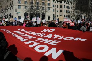 Demonstrators carry a large red banner reading “No Cooperation With the Occupation” as they move from Pennsylvania Avenue toward 15th Street. (André Hiroki/MNS)