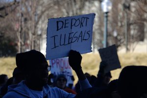 A small group of counter-protesters gathers along Pennsylvania Avenue, holding signs calling for stricter immigration enforcement as demonstrators from the walkout pass nearby. (André Hiroki/MNS)