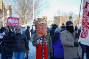 A stick with a Trump mask dressed up as a king was stuck into the snow at the edge of the sidewalk, referencing the “No Kings” movement. (Cayla Labgold-Carroll/MNS)